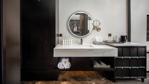 Ein modernes Badezimmer mit einem dunklen Holz-Waschtisch, einer weißen Marmorwaschbecken und einem runden Spiegel mit goldener Rahmung.