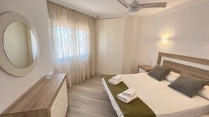 A hotel room with a bed, a bedside table, a mirror, a ceiling fan, and a window with curtains. - Las Pergolas by Interhome (Jávea)