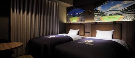 Ein Hotelzimmer mit zwei Betten, jeweils mit einer baseball-bezogenen Tagesdecke, einem großen Fenster mit Blick auf ein Baseballstadion und einem Vorhang auf der linken Seite.