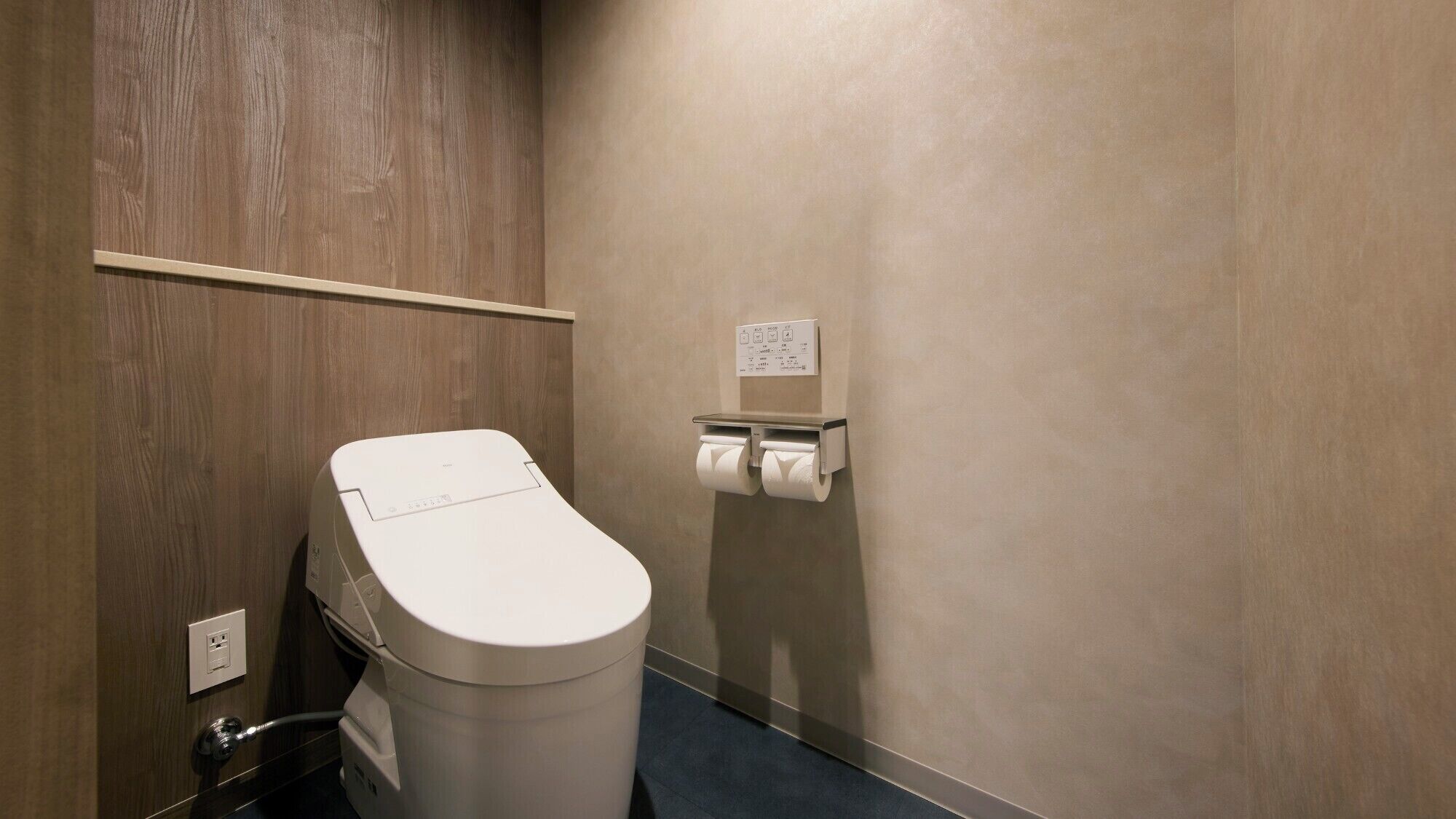 A modern bathroom with a toilet, a paper towel dispenser, and a wooden wall.