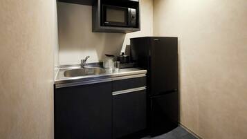 A compact kitchen with a black refrigerator, a microwave above the sink, and a stainless steel sink.