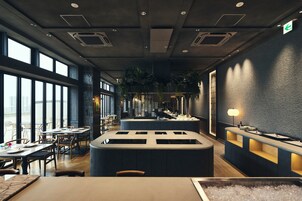 Interior moderno de restaurante com grandes janelas, área de bar central e disposição de mesas.