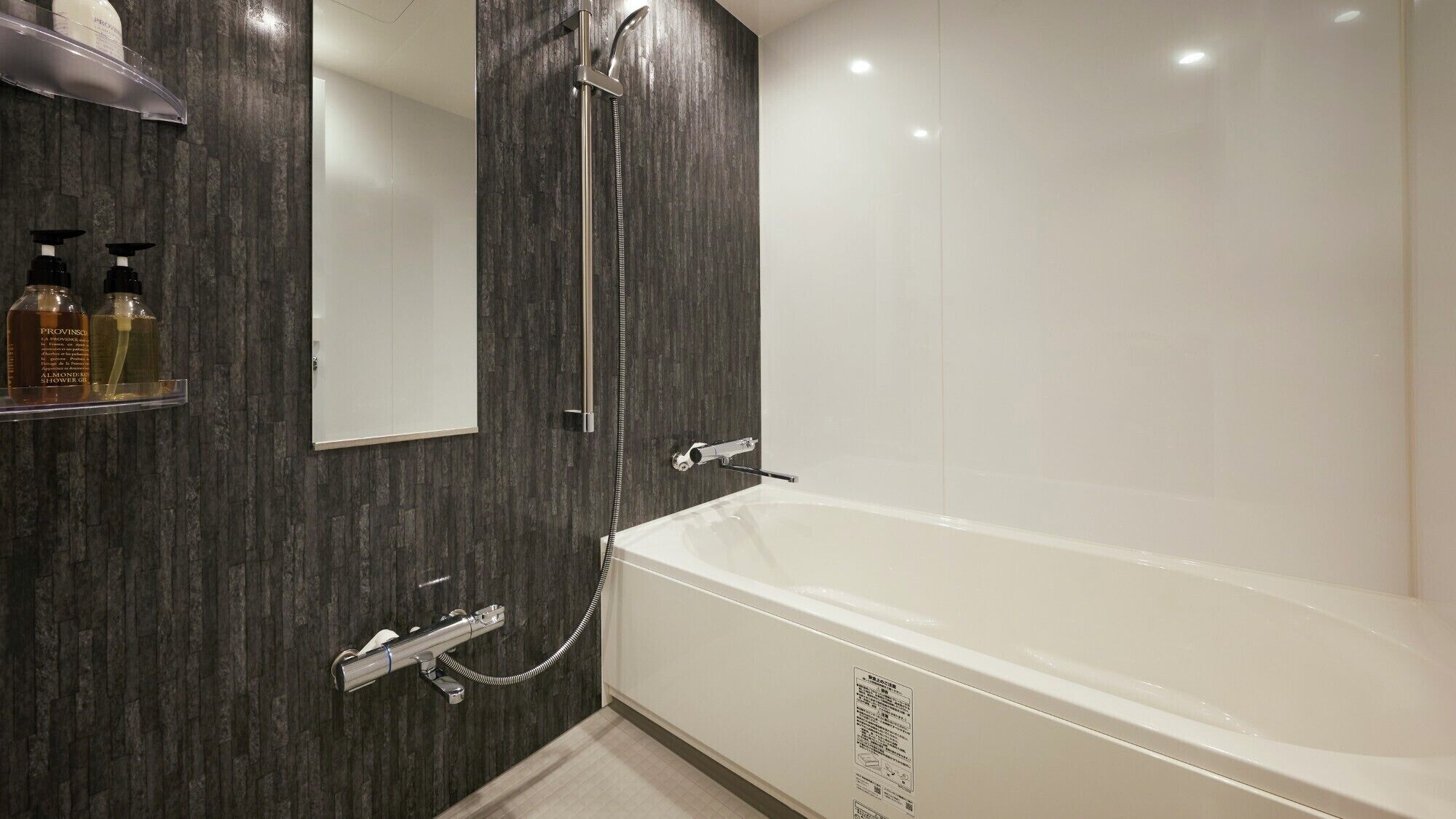 Ein modernes Badezimmer mit einer großen Badewanne, einer Dusche und einem Spiegel. Auf einem Ablagebereich stehen Pflegeprodukte.