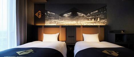 Habitación de hotel con dos camas, cada una con un almohadón que lleva un logotipo. La habitación tiene un cartel grande de un estadio en la pared, y se aprecia una vista del cielo nocturno a través de la ventana.