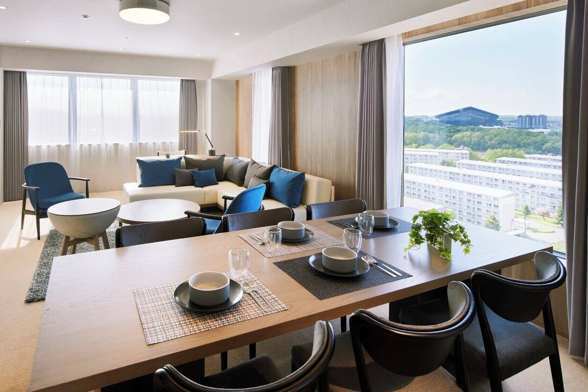 Una habitación de hotel moderna con comedor, un conjunto de sofás y un ventanal con vistas a la ciudad.