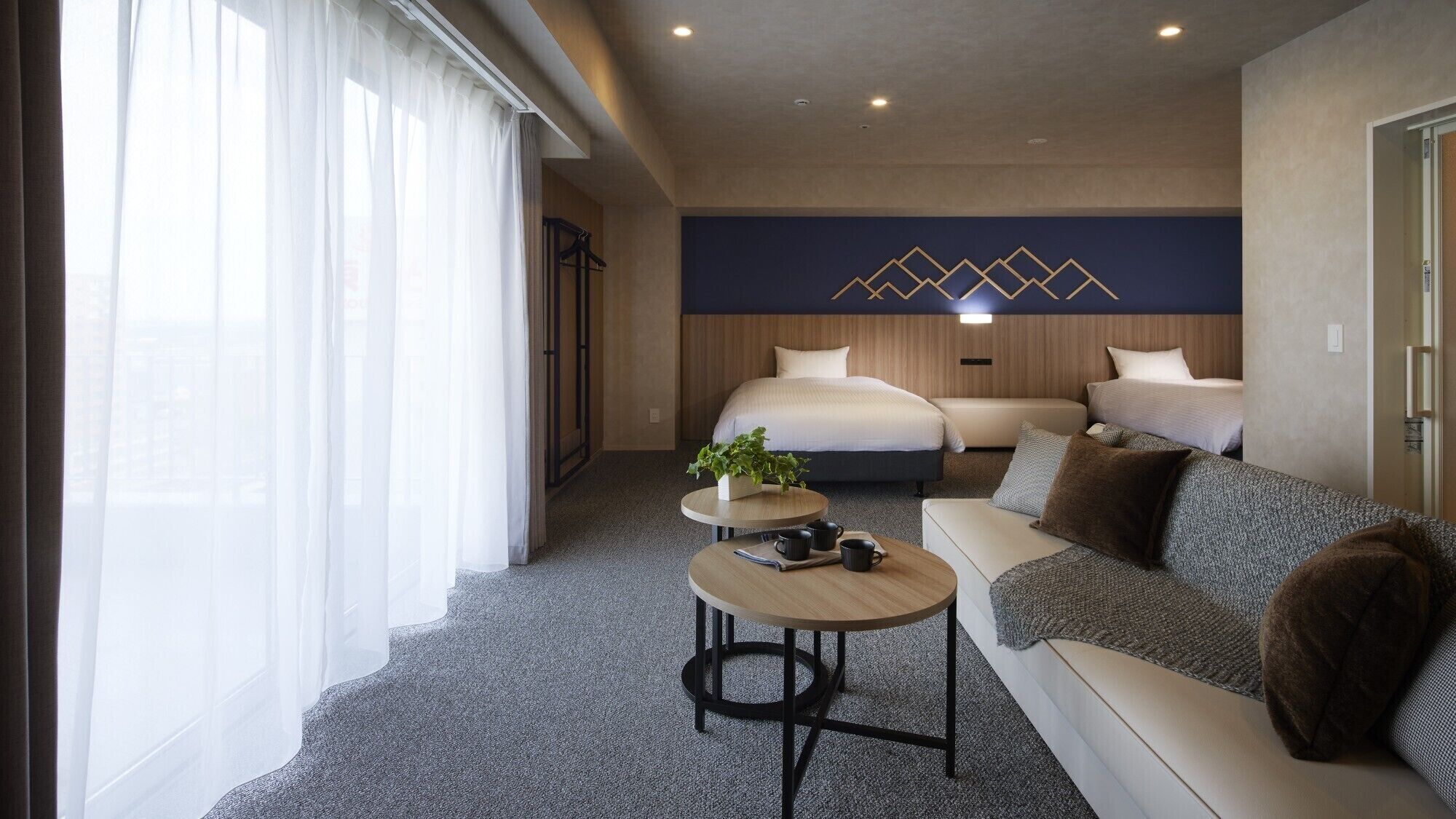 A modern hotel room with a bed, a sofa, a small table with a plant, and a decorative wall.