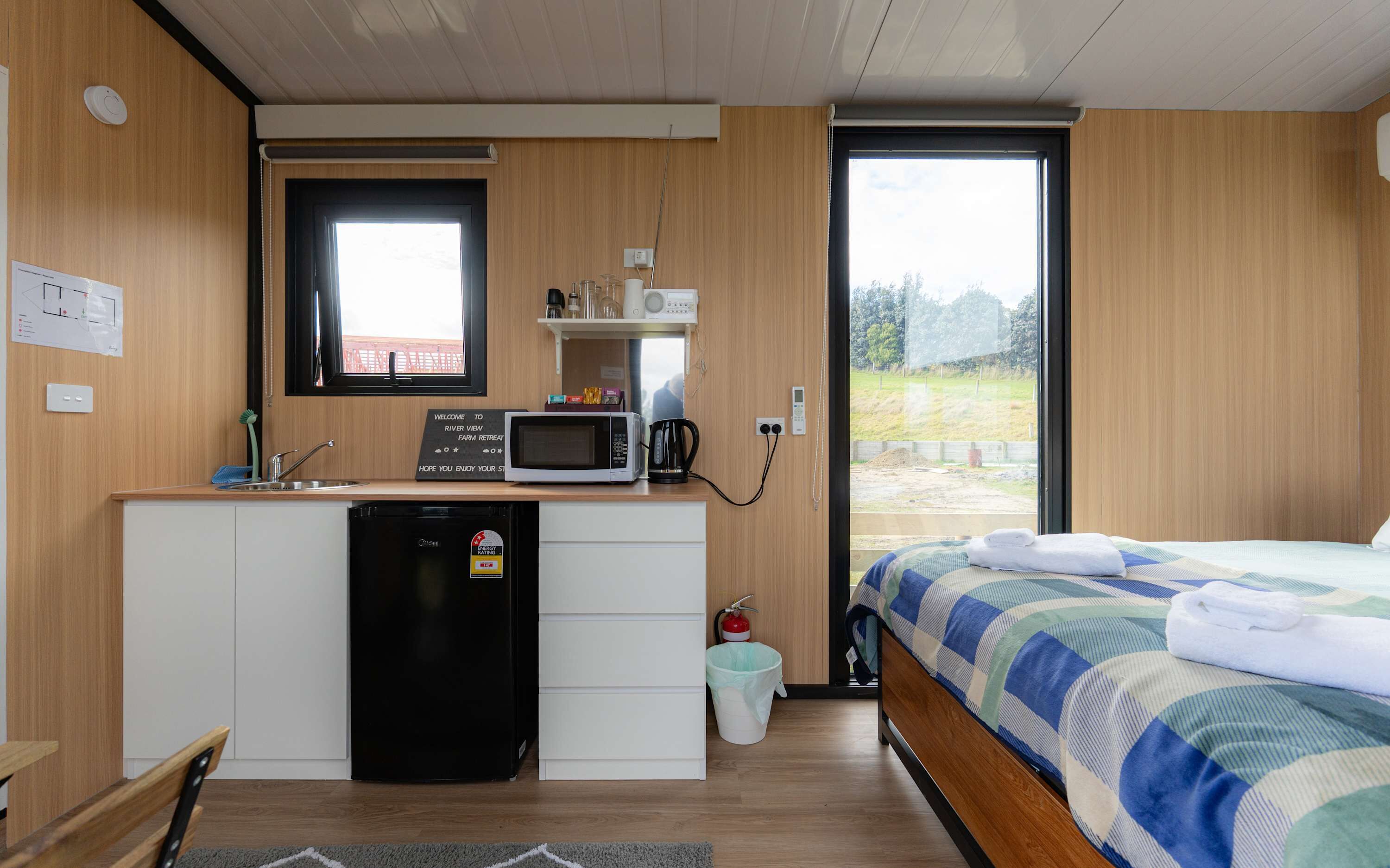 A compact room with a kitchenette, a bed, and a window with a view of a field.