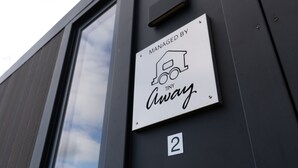 Een bord aan een gevel dat een dienst aangeeft, beheerd door 'Tiny Away', met een icoontje van een huis.