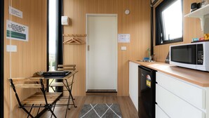 Een kleine keuken met een magnetron, spoelbak en houten keukenkastjes. Er is een zithoekje met een tafel en stoelen.