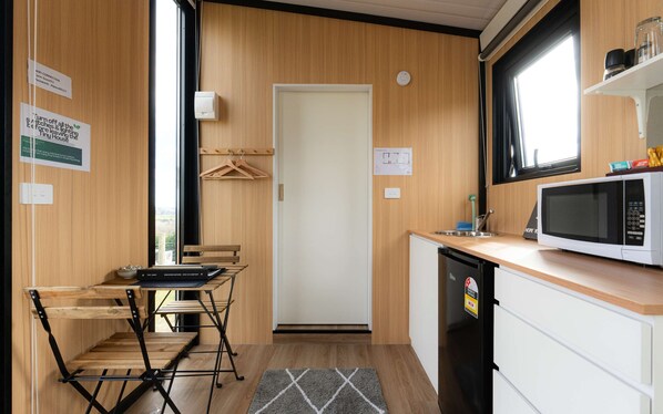 Une cuisine compacte équipée d’un four à micro-ondes, d’un évier et de placards en bois. Un petit coin repas avec une table et des chaises est également disponible.