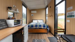 Een compacte, moderne slaapkamer met een bed, een magnetron, een klein bureau en uitzicht op het landschap.