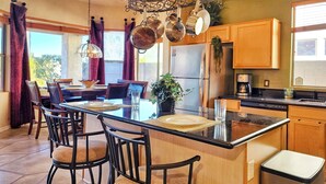 A modern kitchen with a central island, bar stools, and a dining table set for four. - Upgraded Golfer's Oasis! Heated Pool, BBQ, Gate Guarded & Pet Friendly! (Phoenix)