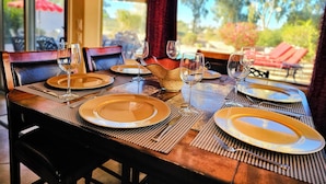 A dining table set with plates, glasses, and cutlery, with a view of outdoor seating and greenery. - Upgraded Golfer's Oasis! Heated Pool, BBQ, Gate Guarded & Pet Friendly! (Phoenix)