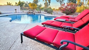 A pool with red lounge chairs and a stone wall. - Upgraded Golfer's Oasis! Heated Pool, BBQ, Gate Guarded & Pet Friendly! (Phoenix)