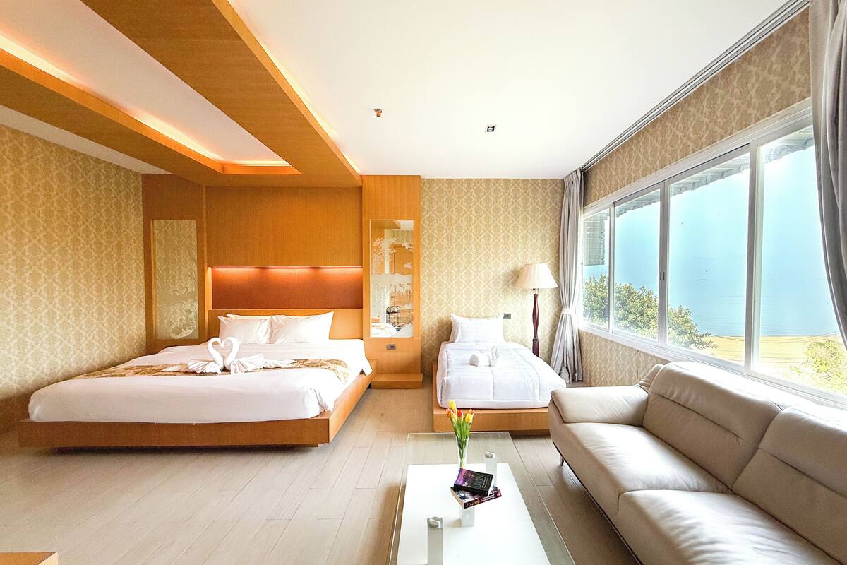 Une chambre d’hôtel avec deux lits, un canapé, une table basse et une grande fenêtre donnant sur un beau paysage.