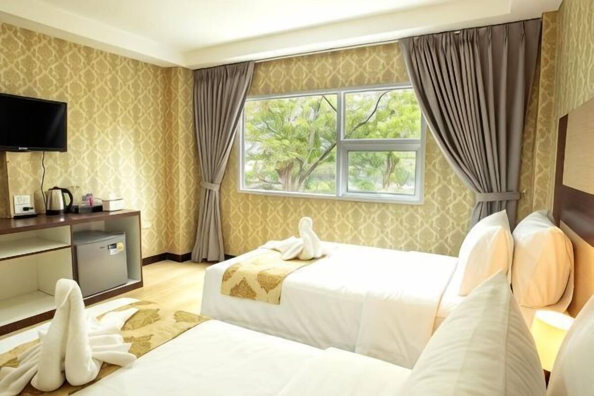 Une chambre d’hôtel avec deux lits, un bureau avec une télévision et une fenêtre avec des rideaux.