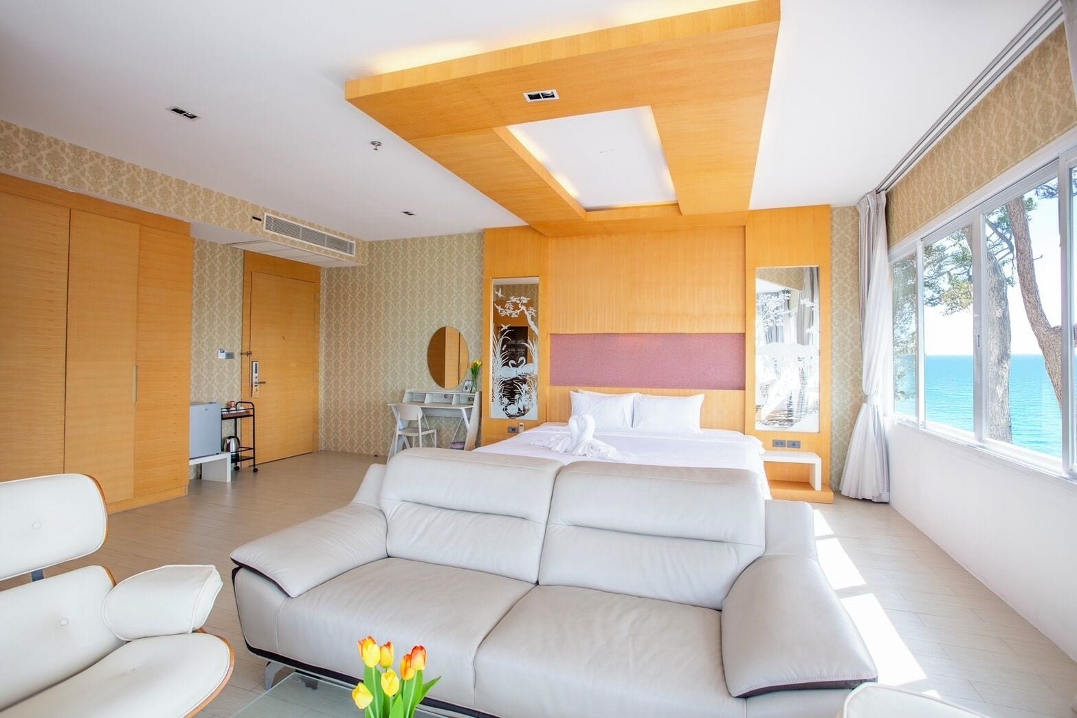 A modern hotel room with a large bed, a sofa, a desk, and a view of the sea.