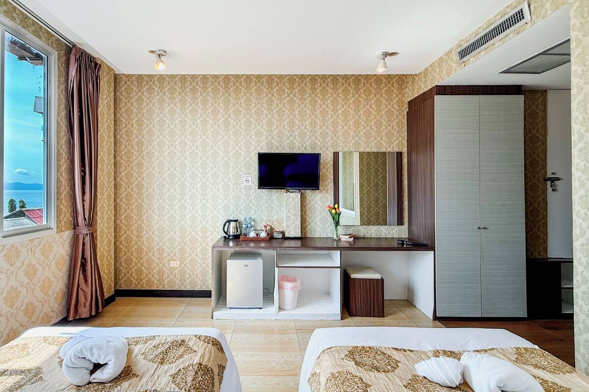 Une chambre d’hôtel avec deux lits, un bureau avec une télévision, une armoire et une vue sur la mer.