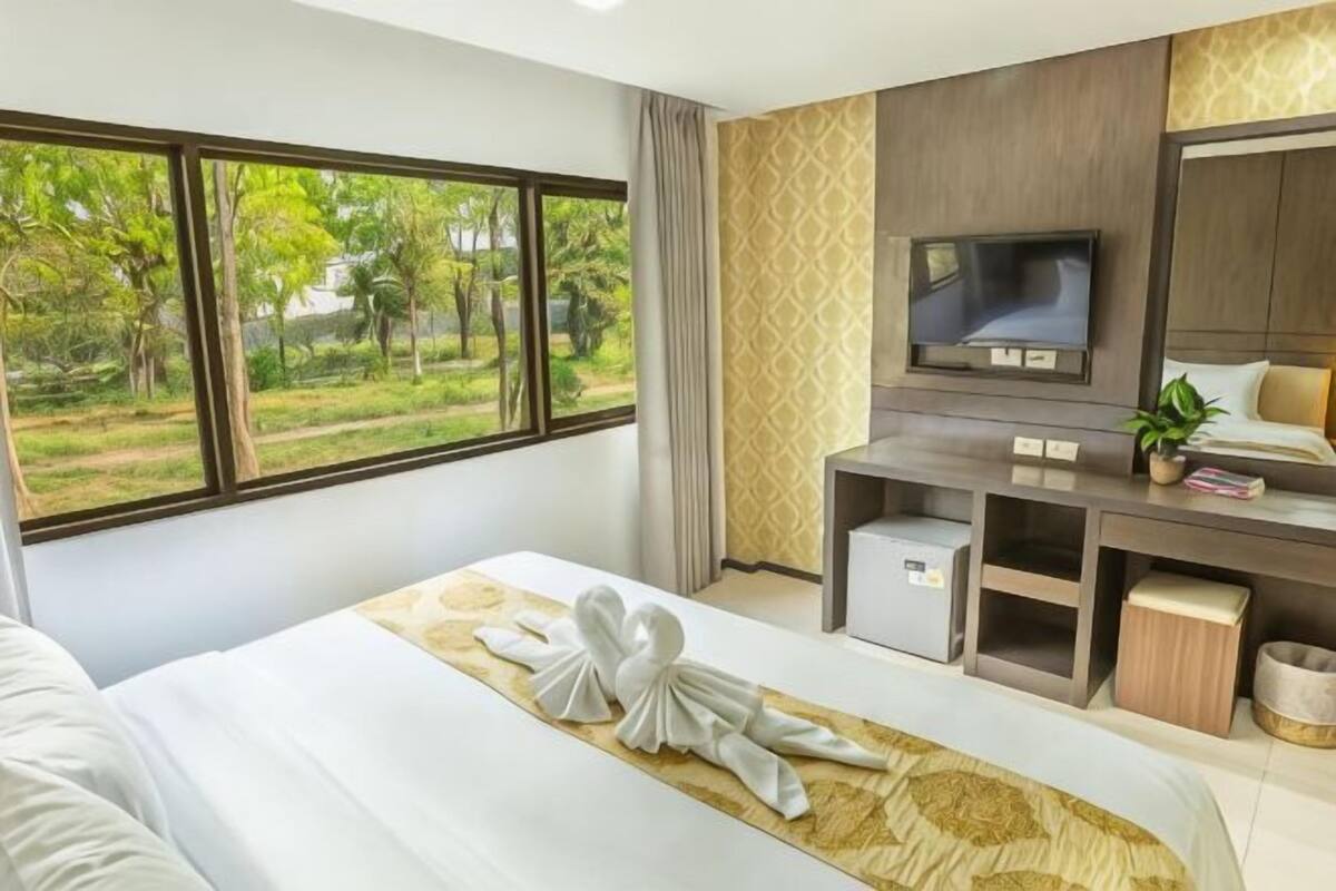 Une chambre d’hôtel avec un grand lit, une télévision, un bureau avec un ordinateur et une vue sur la verdure.