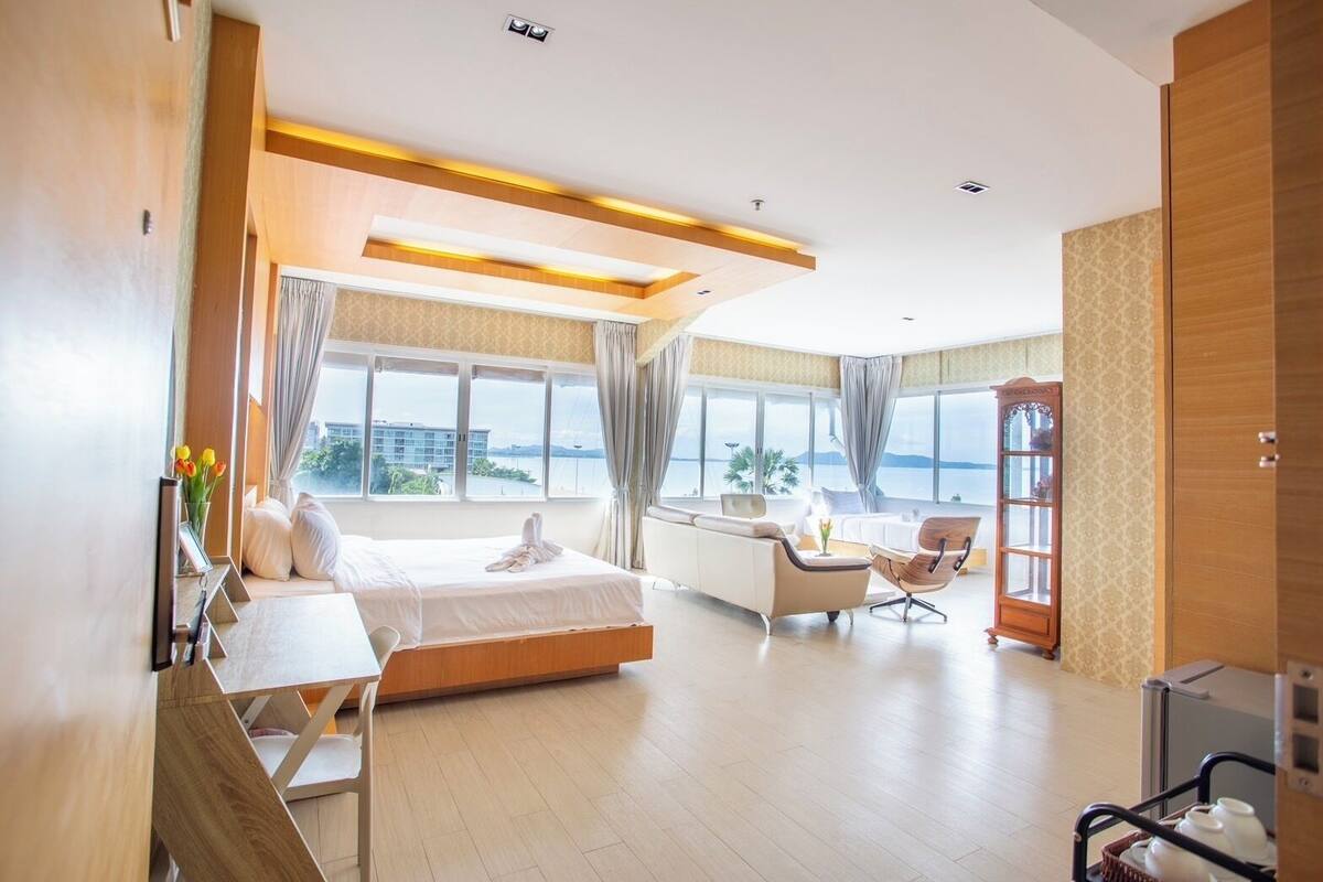 Une chambre d’hôtel moderne dotée d’un grand lit, d’un coin salon avec une table et des chaises, d’une vue sur la mer et d’une grande fenêtre.