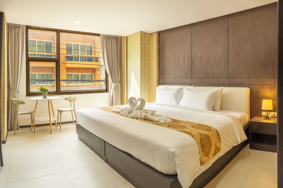 Une chambre d’hôtel avec un grand lit, une petite table avec deux chaises, une fenêtre avec des rideaux et une table de chevet avec une lampe.