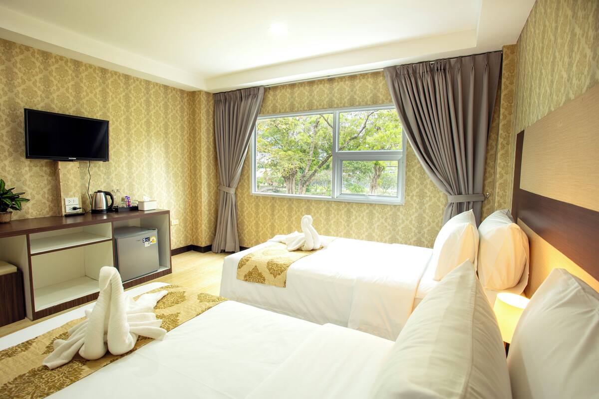Une chambre d’hôtel avec deux lits, une télévision, un bureau avec une bouilloire et une fenêtre avec des rideaux.