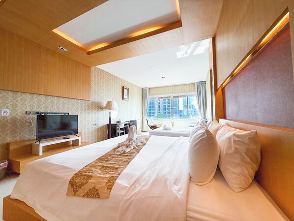 A modern hotel room with a large bed, a flat-screen TV, a desk, and a window with a city view.