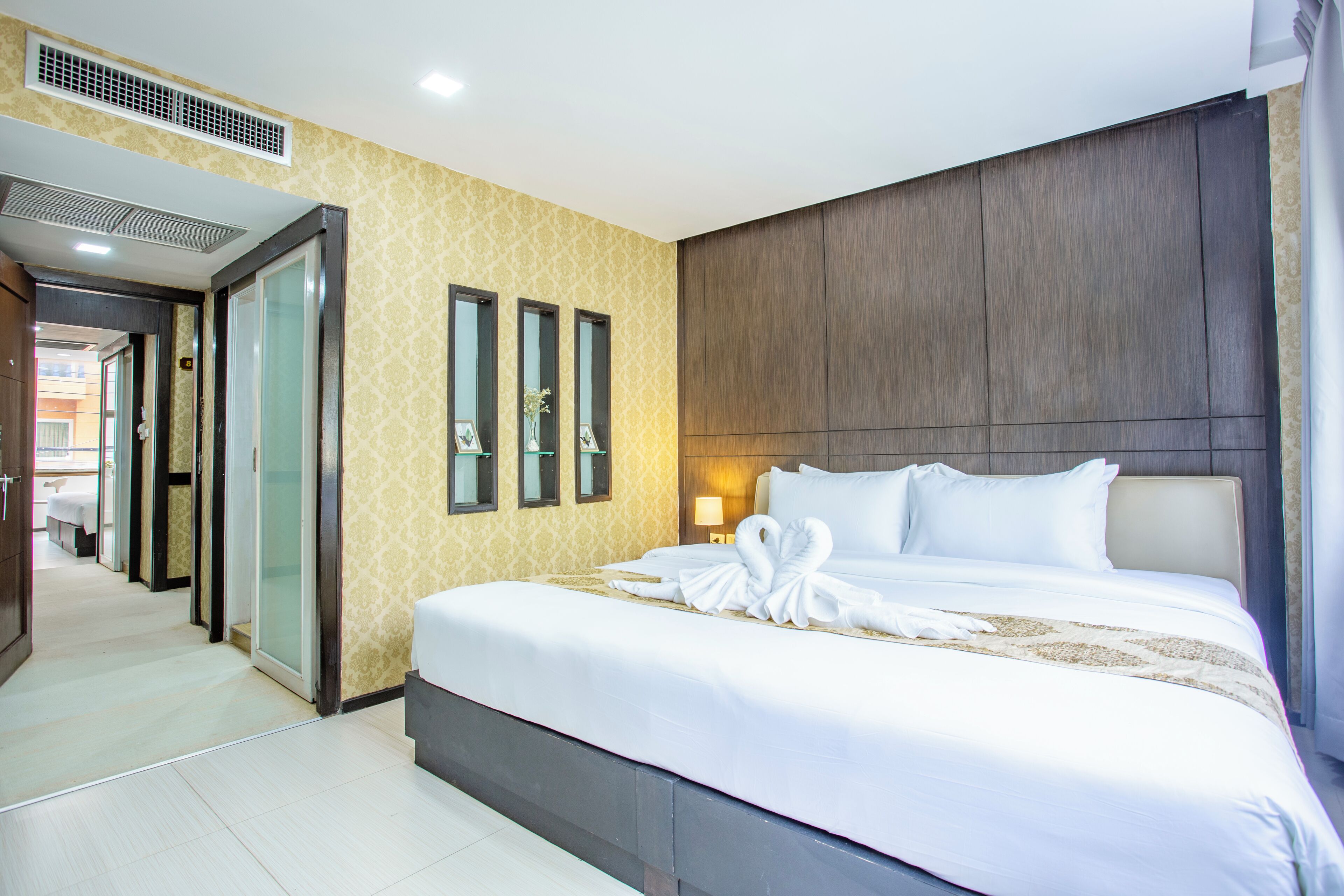 A hotel room with a large bed, a wooden headboard, and a hallway leading to other rooms.