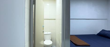 A small, narrow bathroom with a toilet and a shower area.