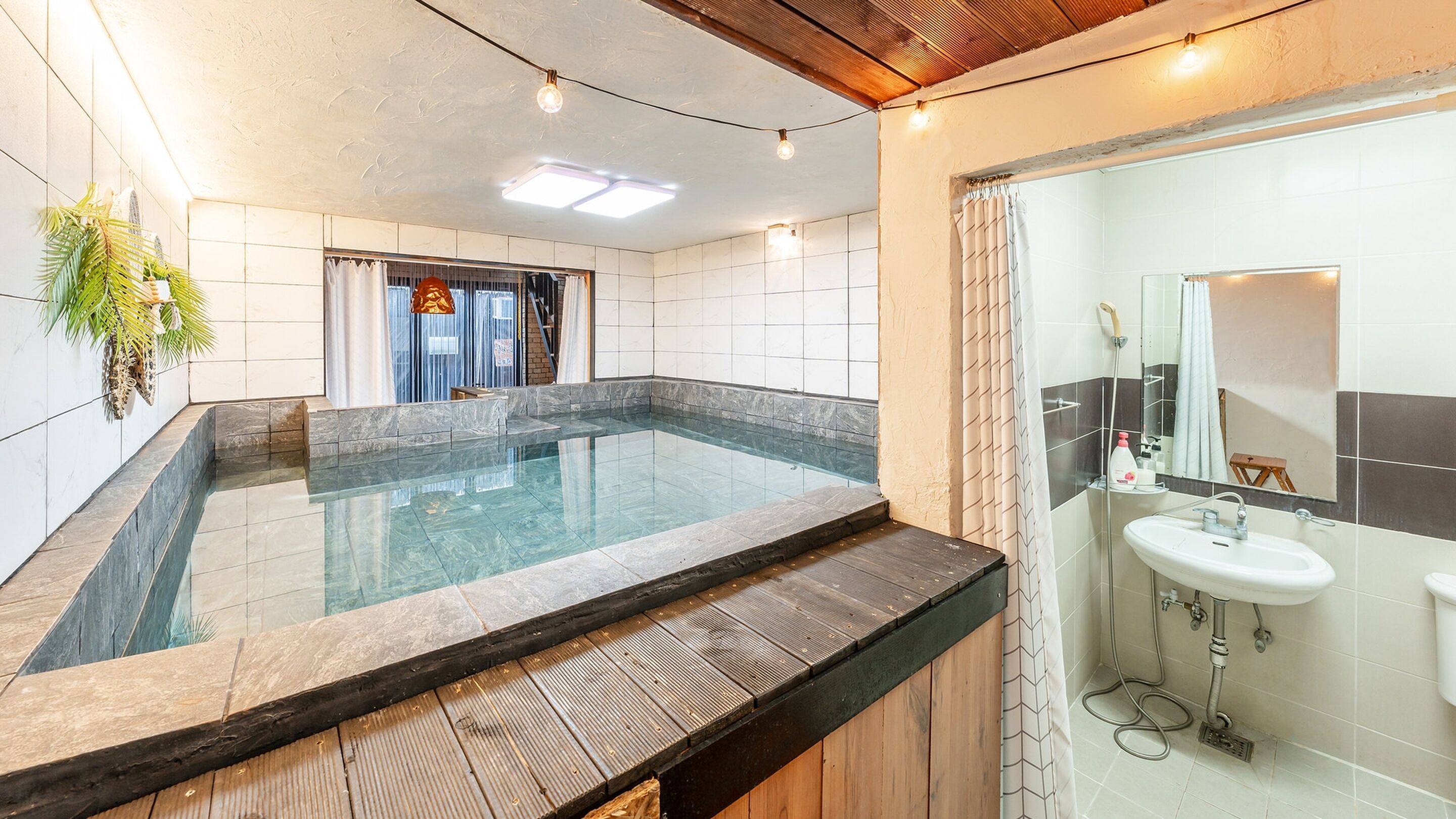 Une salle de bain moderne dotée d’un jacuzzi entouré de parois de verre, d’une terrasse en bois et d’un lavabo blanc avec un miroir.
