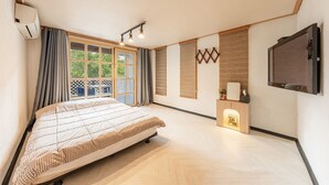 A bedroom with a bed, a window, a wall-mounted TV, and a small wooden cabinet. - Gangchon Afternoon Pool Villa Pension (Chuncheon)