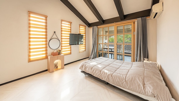 A bedroom with a large bed, a TV mounted on the wall, and a window with blinds. - Gangchon Afternoon Pool Villa Pension (Chuncheon)