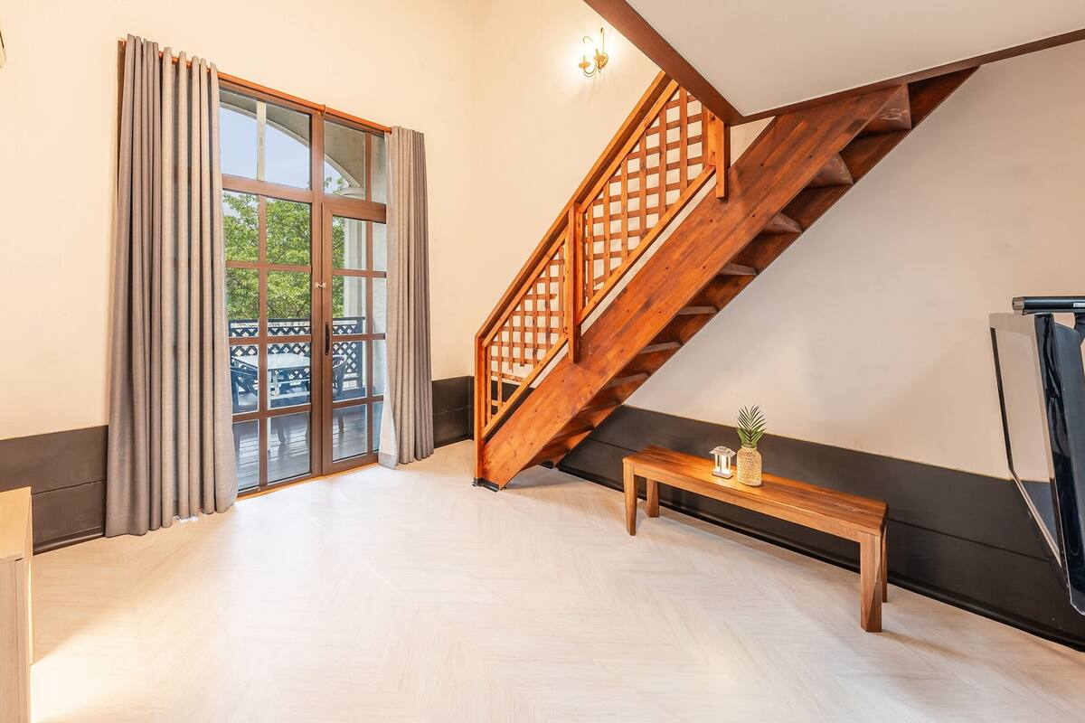 A spacious room with a large sliding glass door leading to an outdoor area, a wooden staircase, and a small wooden bench.