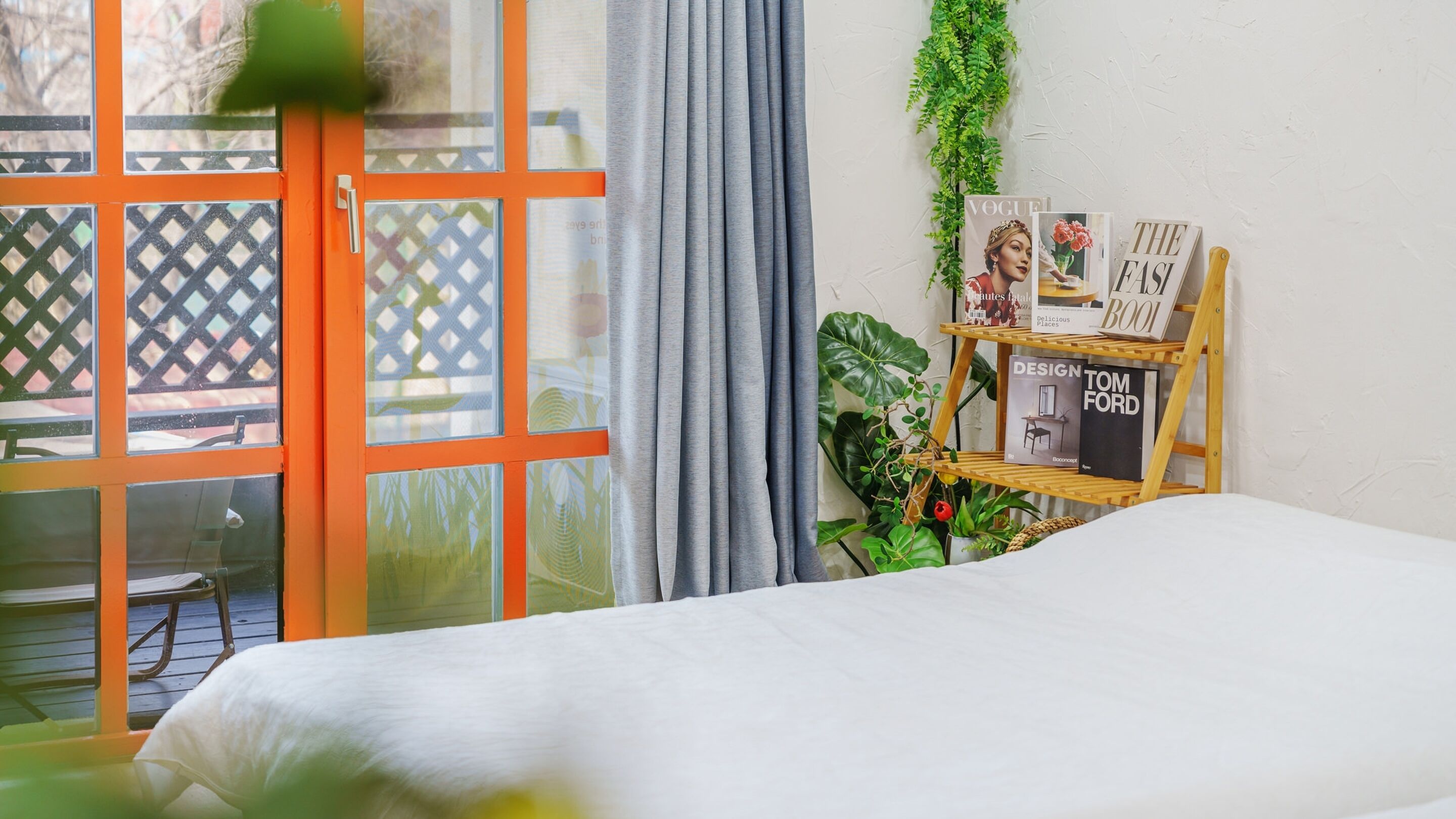 Una habitación con una cama, una ventana con cortinas, una escalera de madera y un estante con libros y revistas.