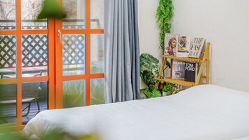 Una habitación con una cama, una ventana con cortinas, una escalera de madera y un estante con libros y revistas.