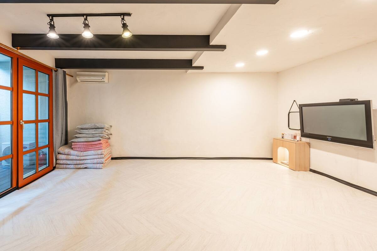 A spacious room with a large window, a flat-screen TV, and a stack of folded blankets.