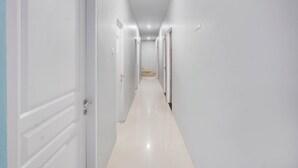 A long, narrow hallway with white walls and doors, leading to a staircase. - Hotel O Panakukkang Near Mall Panakkukang Formerly Hawai Inn (Makassar)