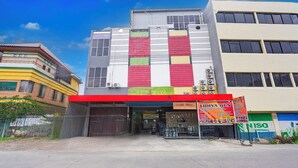 A multi-story building with a red and white facade, a visible storefront with a sign, and a gated entrance. - Hotel O Panakukkang Near Mall Panakkukang Formerly Hawai Inn (Makassar)