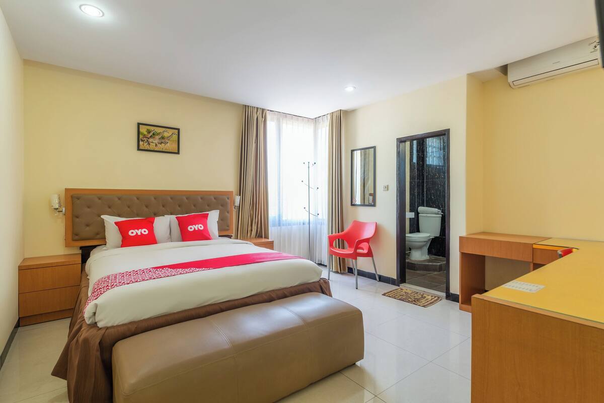 A hotel room with a large bed, a desk, a chair, and a bathroom visible through an open door.