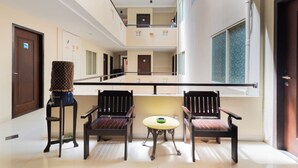Een ruime gang met een hoge plafond, een centraal zithoek met een ronde tafel, en een uitzicht op de bovenverdieping door een glazen balustrade.
