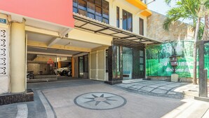 Een hotelentree met een overdekte parkeerplaats, een palmboom en een grote groene banner met tekst.