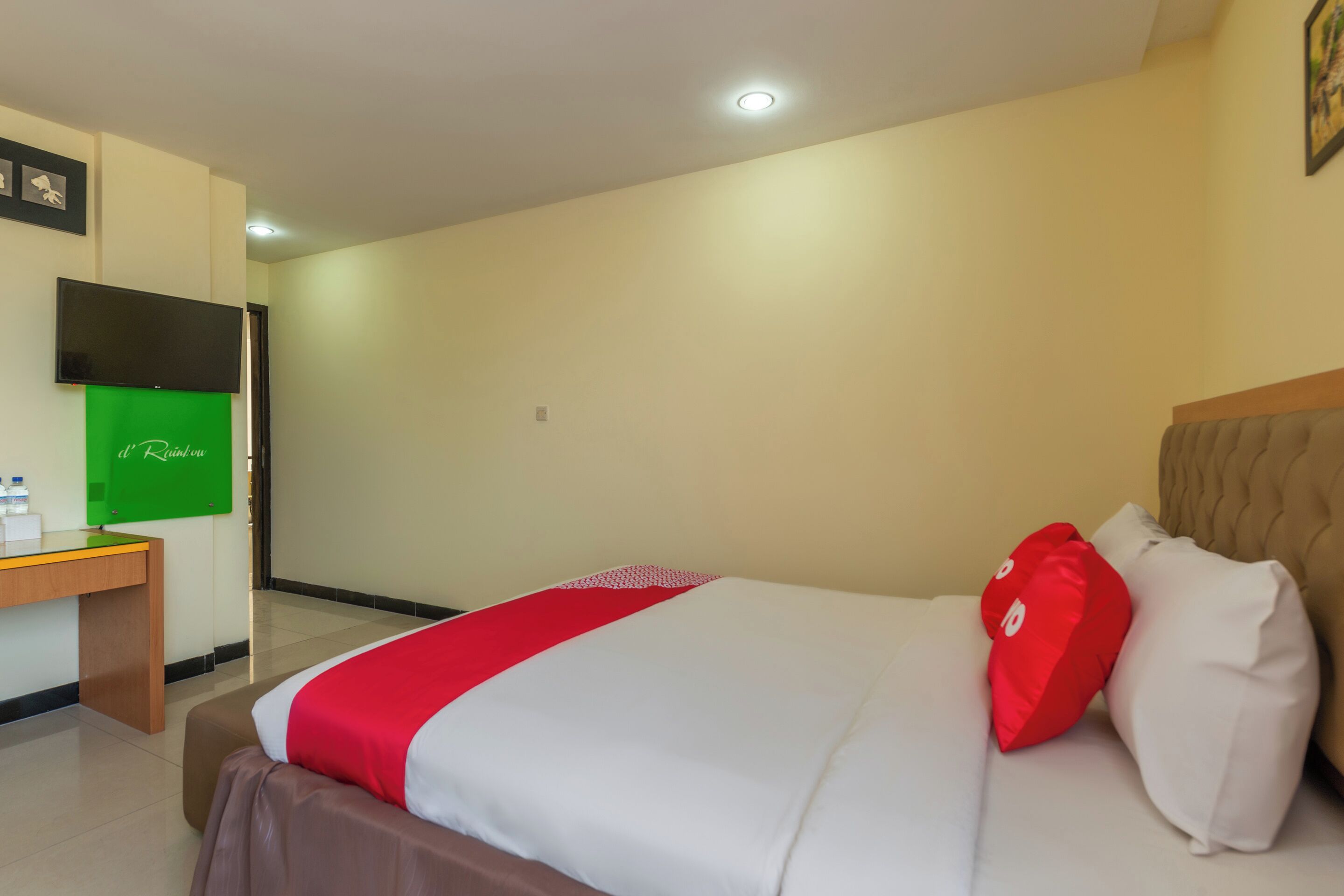 A hotel room with a bed, a desk, a television, and a green sign on the wall.
