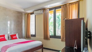 Een hotelkamer met een bed, een televisie, een raam met gordijnen en een wandairconditioning.