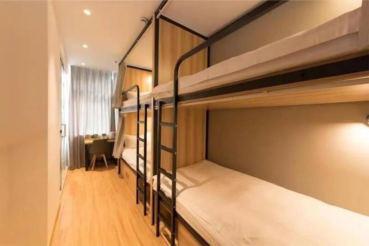 A bunk bed room with a desk and chair, wooden flooring, and curtains.