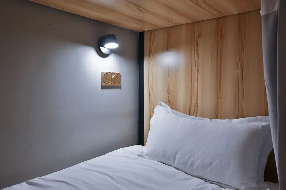 Een slaapkamer met een houten hoofdeinde, een wandlamp en een speaker.
