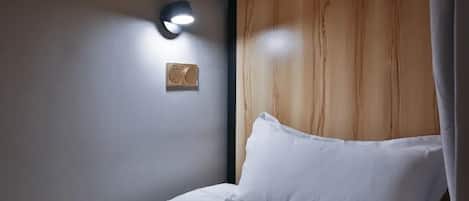 Een slaapkamer met een houten hoofdeinde, een wandlamp en een speaker.