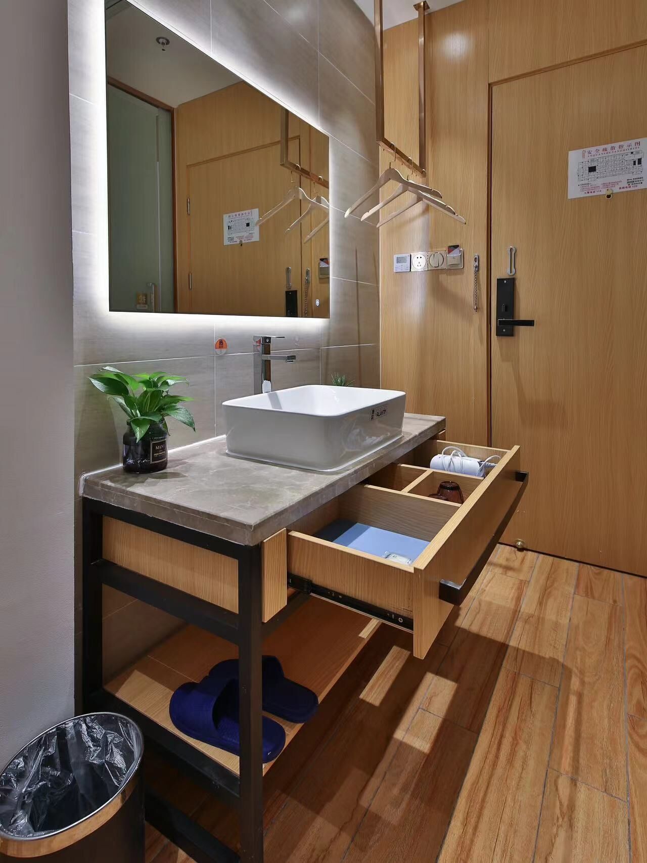 A modern bathroom with a large mirror, a sink with a marble countertop, wooden cabinets, and a built-in shoe rack.
