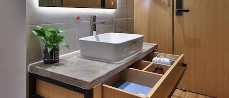 A modern bathroom with a large mirror, a sink with a marble countertop, wooden cabinets, and a built-in shoe rack.
