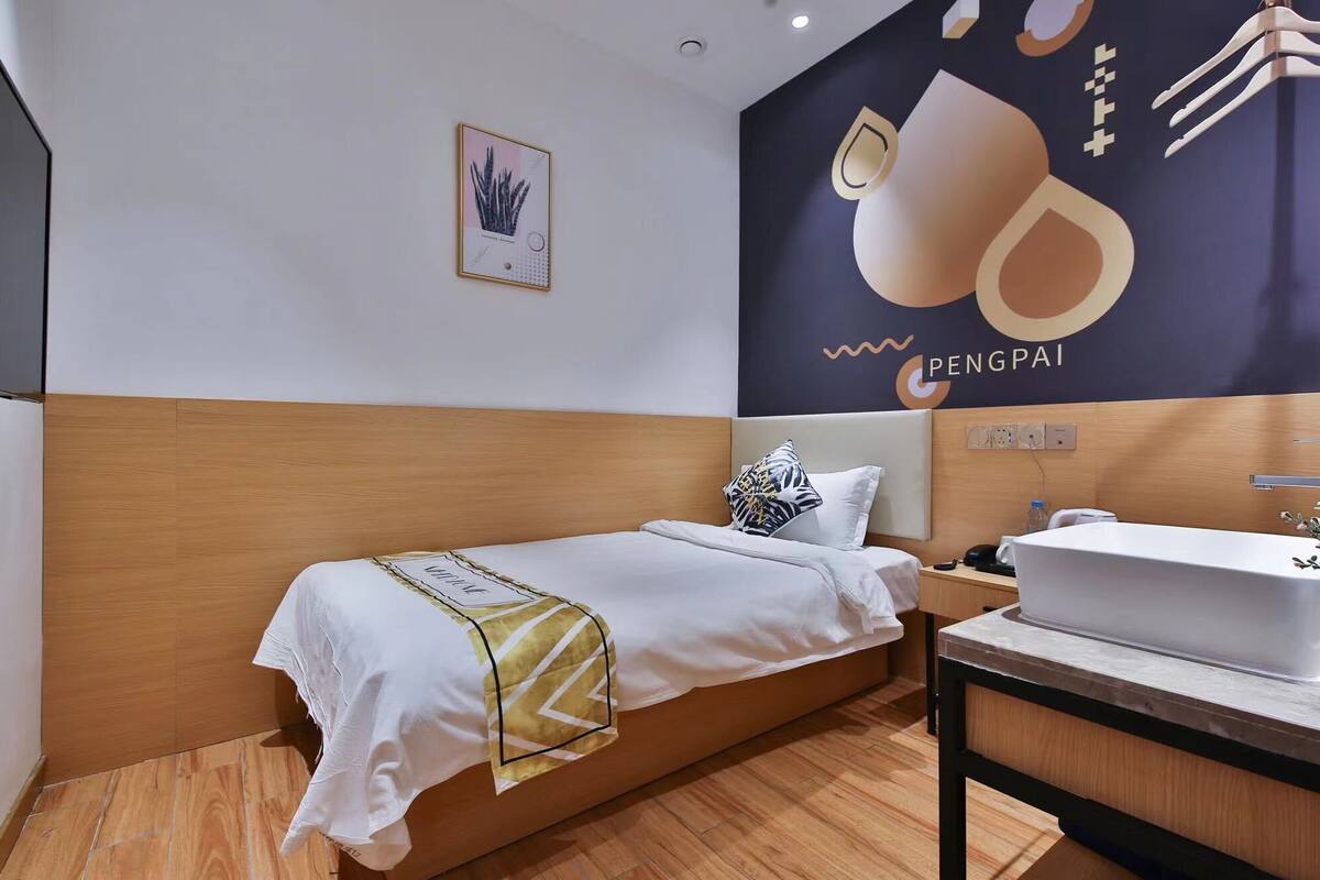 A hotel room with a bed, a nightstand, a sink, and a wall with a large poster.
