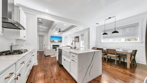 A modern kitchen with white cabinetry, a central island, and a dining area with wooden chairs and a table.